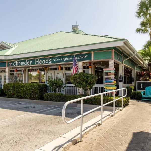 Exterior of Chowder Heads restaurant with a green roof, white railing, and palm trees.