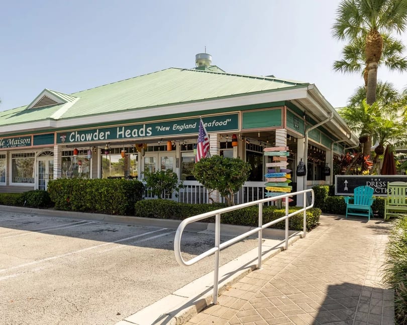 Exterior of Chowder Heads restaurant with a green roof, white railing, and palm trees.