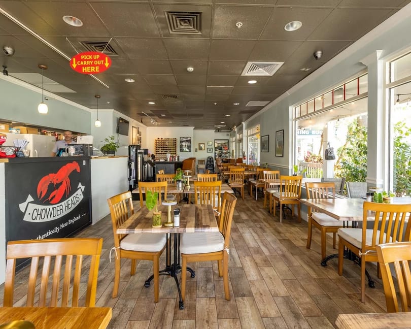 Interior of Chowder Heads restaurant with wooden tables and chairs, a counter, and large windows.
