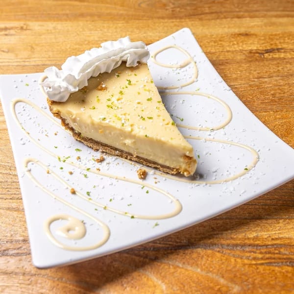Slice of key lime pie with whipped cream and lime zest on a white plate.