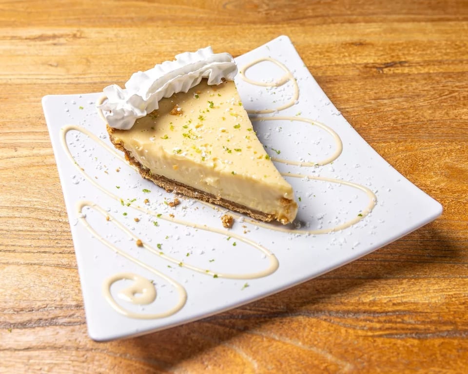 Slice of key lime pie with whipped cream and lime zest on a white plate.