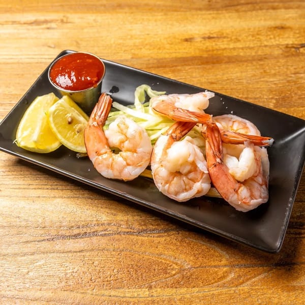 Shrimp cocktail with lemon wedges, cocktail sauce, and shredded lettuce on a black plate.