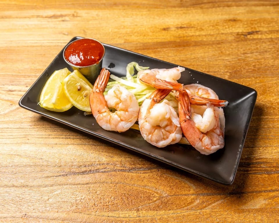 Shrimp cocktail with lemon wedges, cocktail sauce, and shredded lettuce on a black plate.