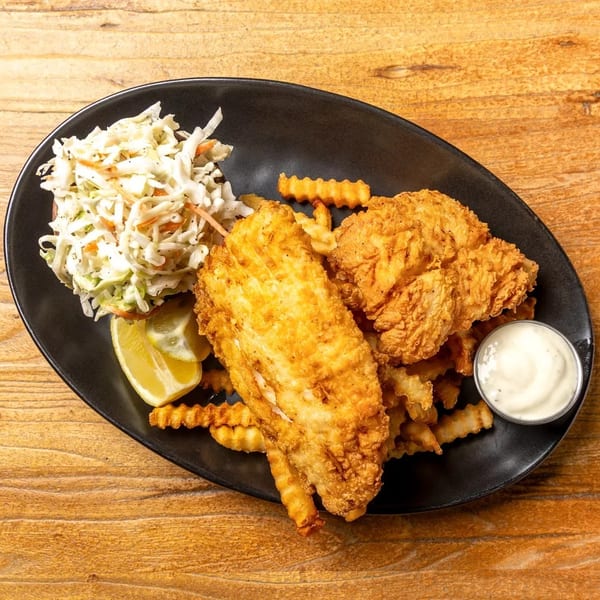 Fried fish and chicken tenders with crinkle-cut fries, coleslaw, lemon, and tartar sauce.
