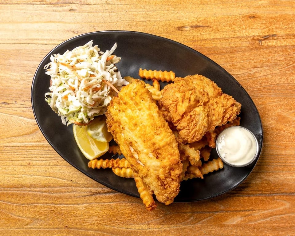 Fried fish and chicken tenders with crinkle-cut fries, coleslaw, lemon, and tartar sauce.