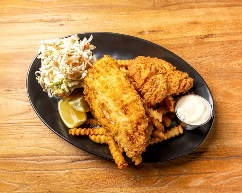 Crispy fried fish and chicken tenders with crinkle-cut fries, coleslaw, lemon, and dipping sauce.